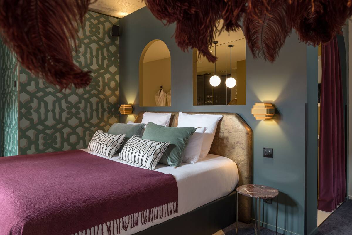 A bedroom with a large bed, patterned wallpaper, a mirror, and a small round table.