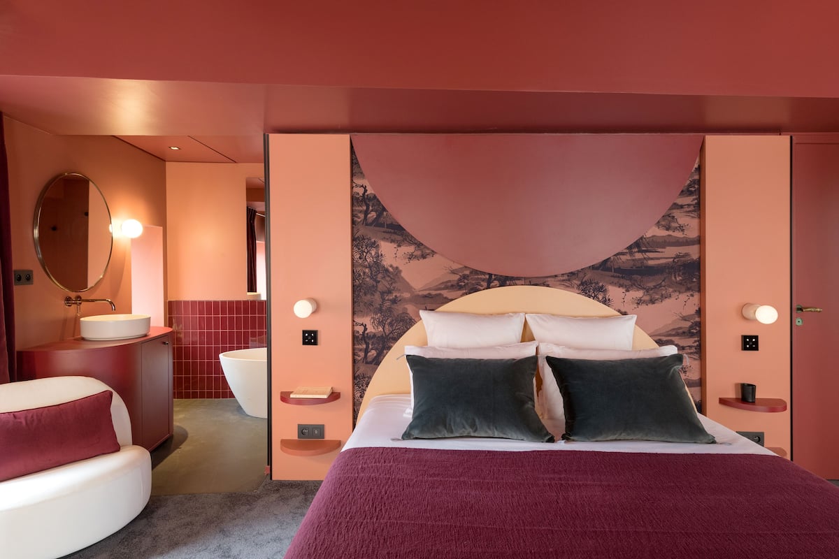 A bedroom with a large bed, a round mirror, a sink, and a toilet.
