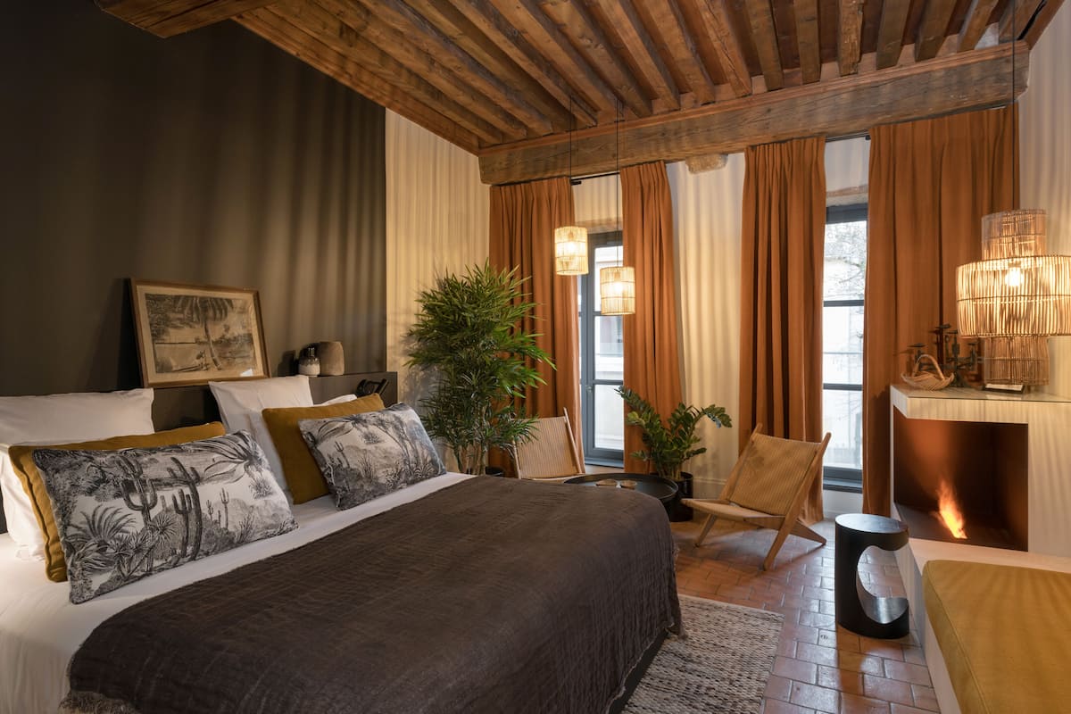 A bedroom with a large bed, a wooden ceiling, a fireplace, and a view of the outdoors.
