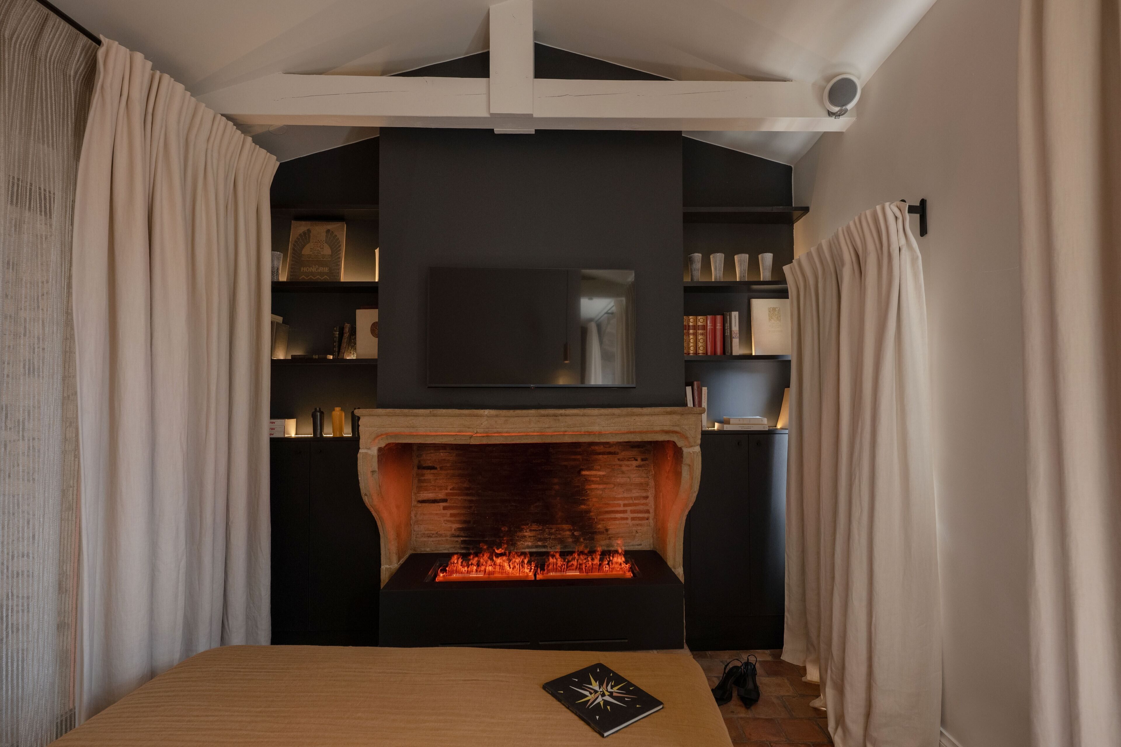 Une pièce avec une cheminée, un lit, un téléviseur placé au-dessus de la cheminée et une bibliothèque.