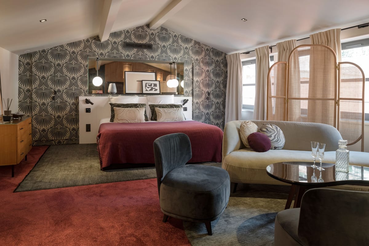 A bedroom with a bed, a sofa, a chair, a table, and a mirror.