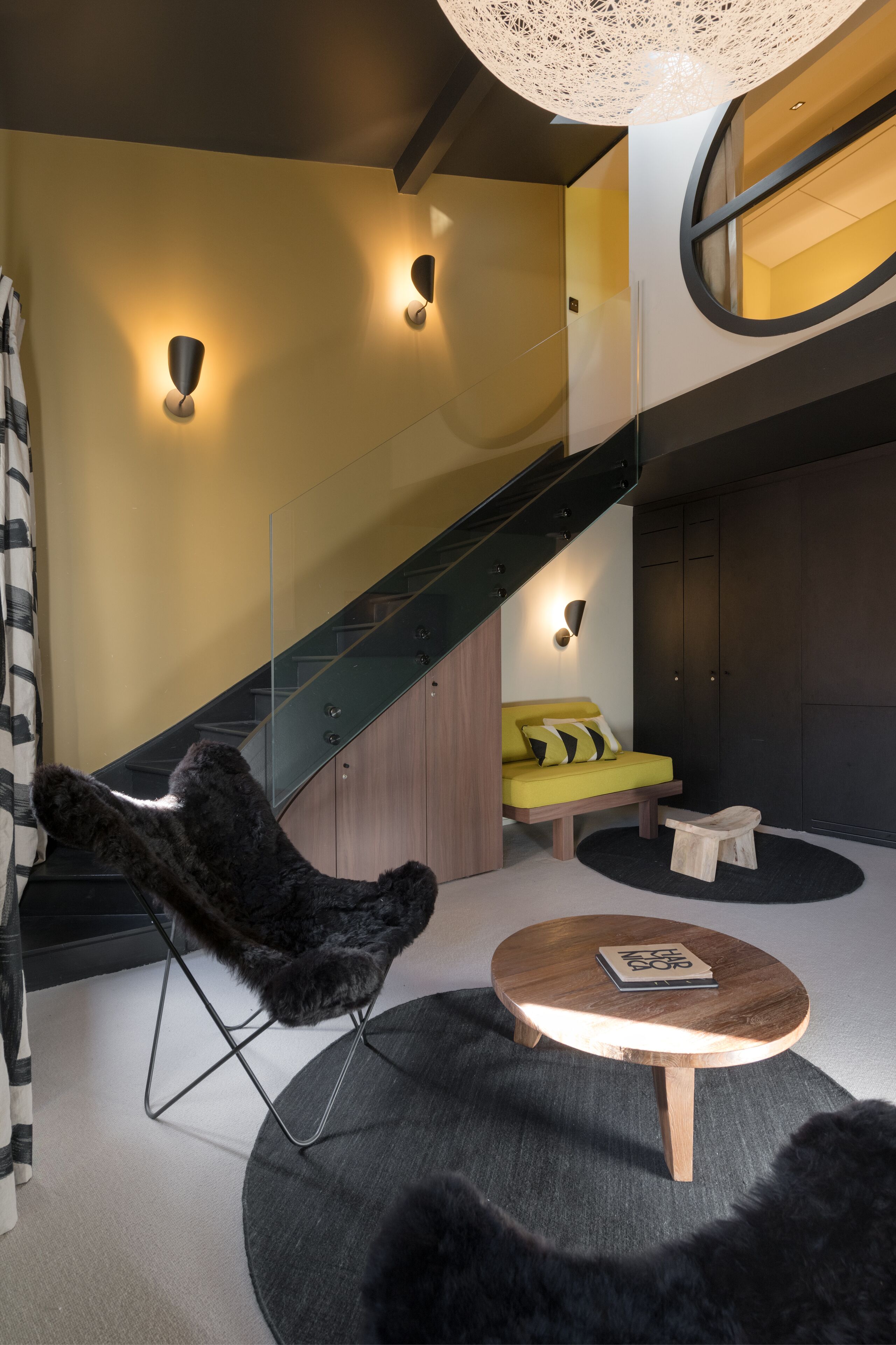 Un intérieur moderne avec un escalier, un canapé, une table ronde en bois et un fauteuil noir à la texture duveteuse.