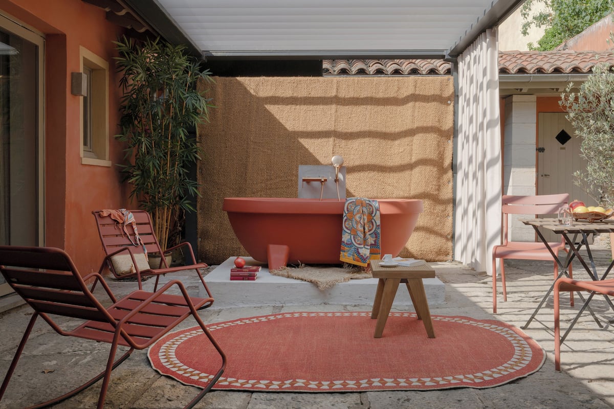 A patio with a red chair, a small table, and a red rug.