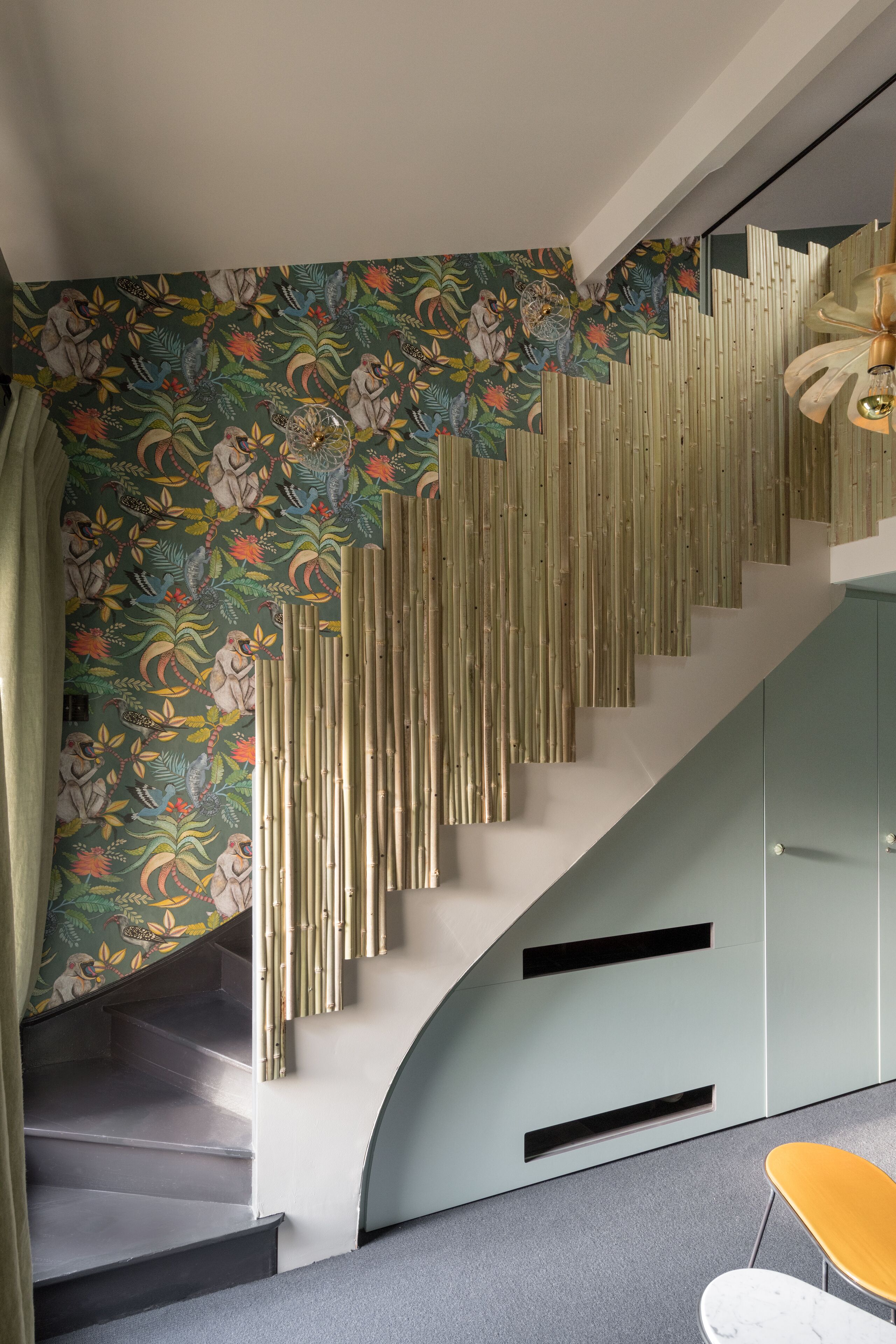 Eine Treppe mit geschwungener Form, eine Wand mit Blumenmuster und eine moderne Leuchte.