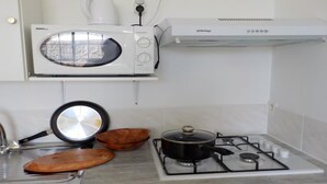 Une cuisine équipée d’un four à micro-ondes, d’une cuisinière à gaz, d’une poêle et de bols en bois.