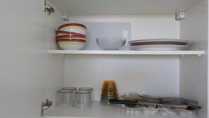 Un meuble de cuisine avec des étagères où sont rangés de la vaisselle, une planche à découper et des ustensiles.