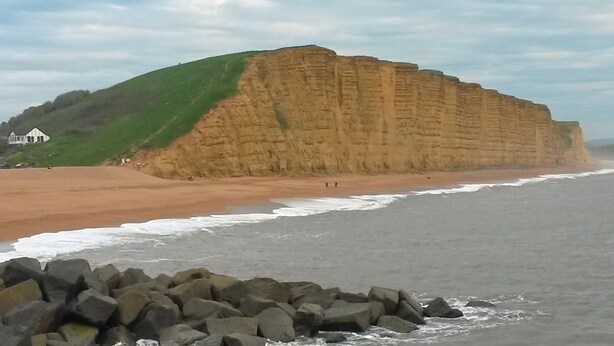 A coastal landscape with a prominent cliff, a sandy beach, and a rocky foreground.
