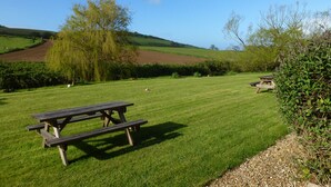 A picnic area with benches and a grassy field, surrounded by trees and hills.