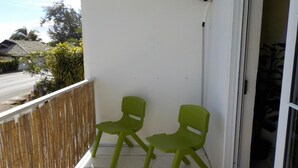 Ein Balkon mit zwei grünen Stühlen, einer weißen Wand und Blick auf eine Straße mit Häusern und Bäumen.