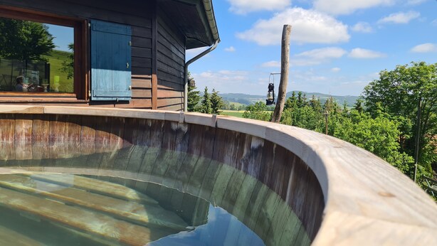 A wooden deck with a swimming pool, a wooden cabin with a blue door, and a view of the landscape.