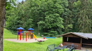 A playground with slides and climbing structures, surrounded by a grassy area and trees.