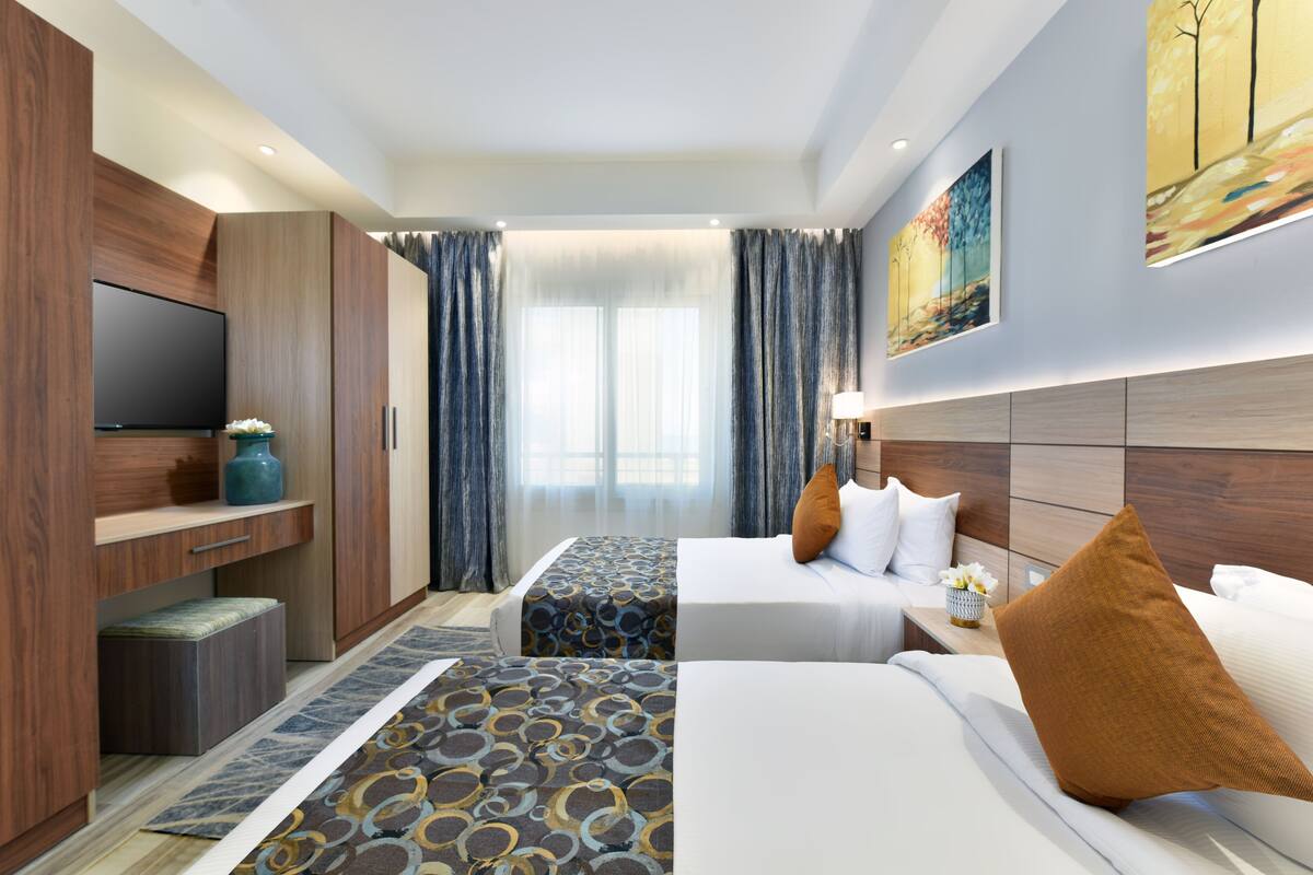 Een hotelkamer met een televisie, twee bedden, een bureau en een groot raam met gordijnen.