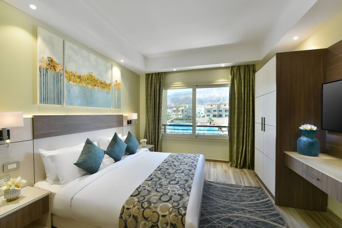 Een hotelkamer met een groot bed, uitzicht op gebouwen door het raam en een televisie aan de rechterkant.