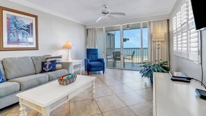 Una sala de estar con un sofá, una mesa de centro, un sillón azul, un televisor y un balcón con vistas.