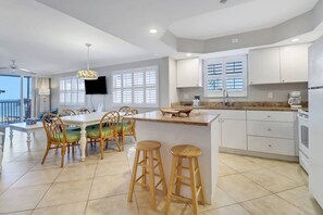 A modern kitchen with white cabinets, a marble countertop, and a dining area with wicker chairs and a table.