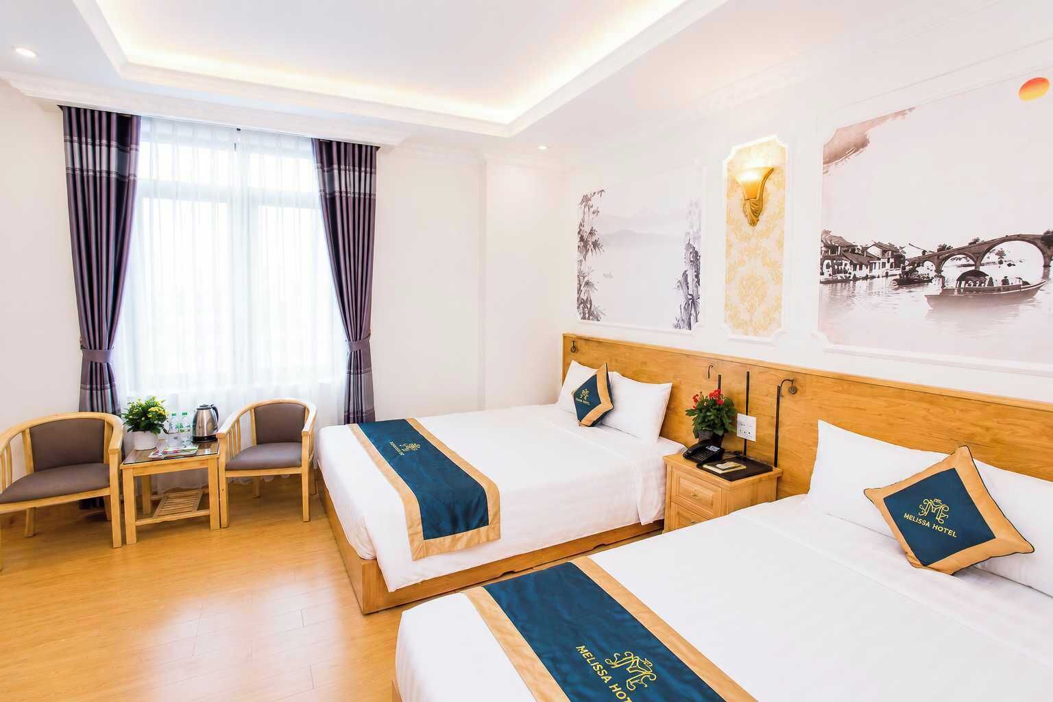 A hotel room with two beds, a small table with chairs, a nightstand with a phone, and a window with curtains.