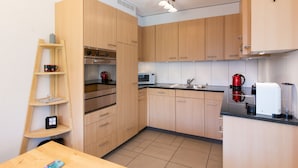 Eine kompakte Küche mit Holzschränken, einem Edelstahlbackofen, einer Mikrowelle, einer Kaffeemaschine und einem Spülbecken.
