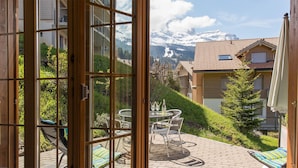 Eine Terrasse mit Tisch und Stühlen, einer Weinflasche und Gläsern, mit Blick auf eine gebirgige Landschaft.
