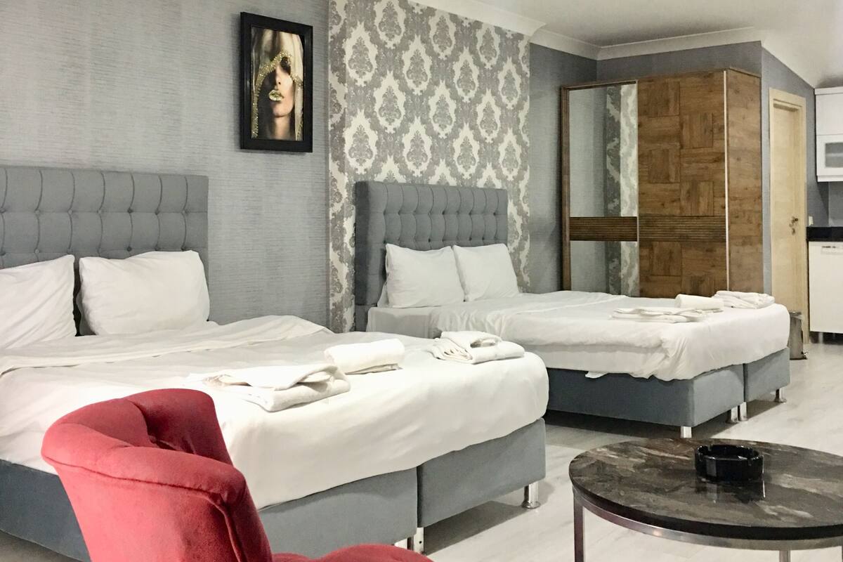A hotel room with two beds, a red chair, a small round table, and a wardrobe.