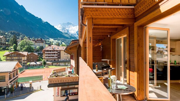 A wooden balcony with a view of a mountain and a restaurant below. - Chalet Belmont - perfect location, recently new (Wengen)