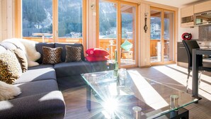 A modern living room with a sectional sofa, a glass coffee table, and large sliding glass doors leading to a balcony. - Chalet Belmont - perfect location, recently new (Wengen)