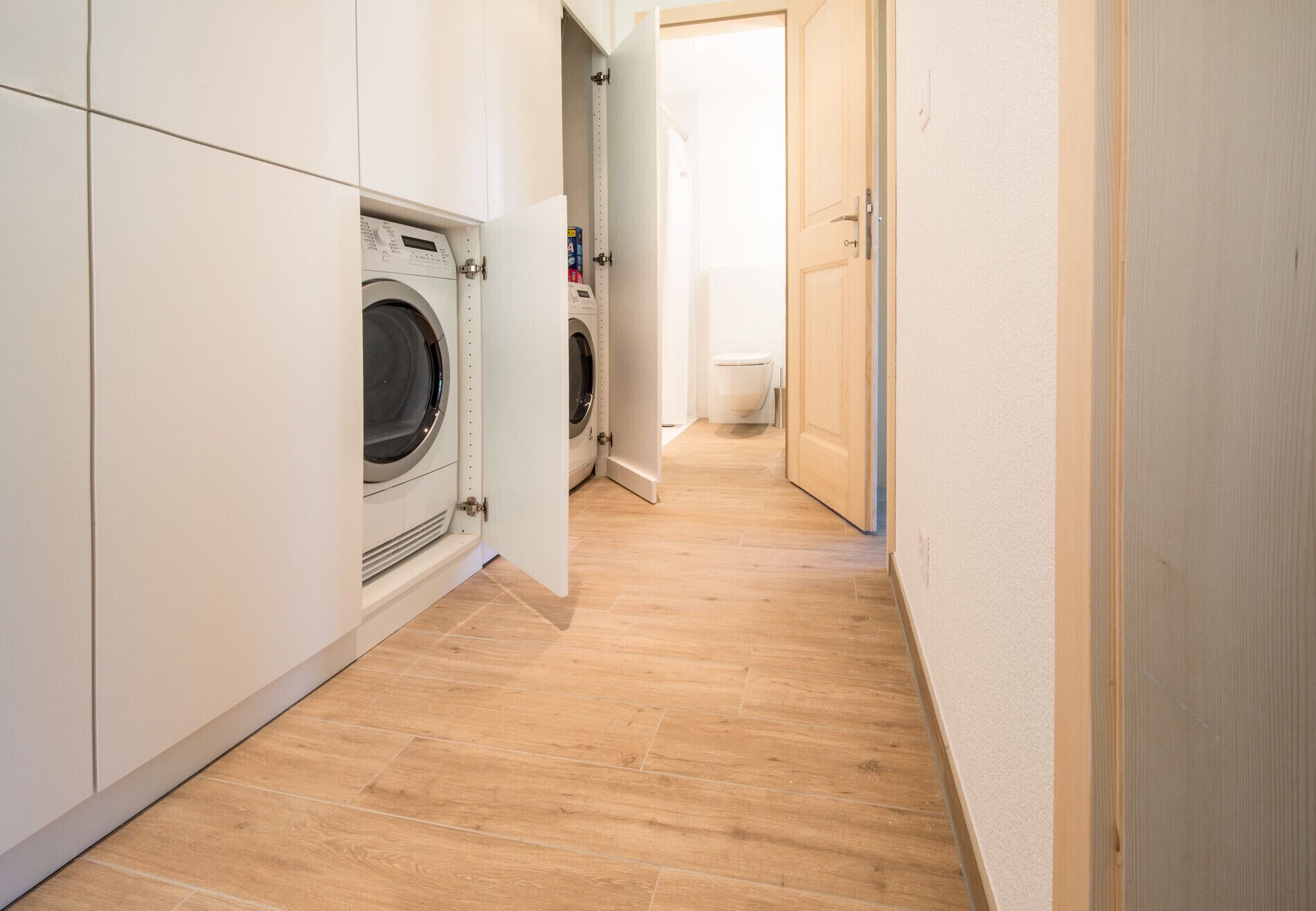 Une buanderie équipée d’un lave-linge et d’un sèche-linge, avec un plancher en bois et une porte donnant sur une salle de bain.