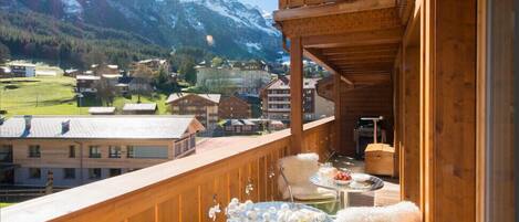 Een houten balkon met een tafel en stoelen, met uitzicht op een bergachtig landschap.