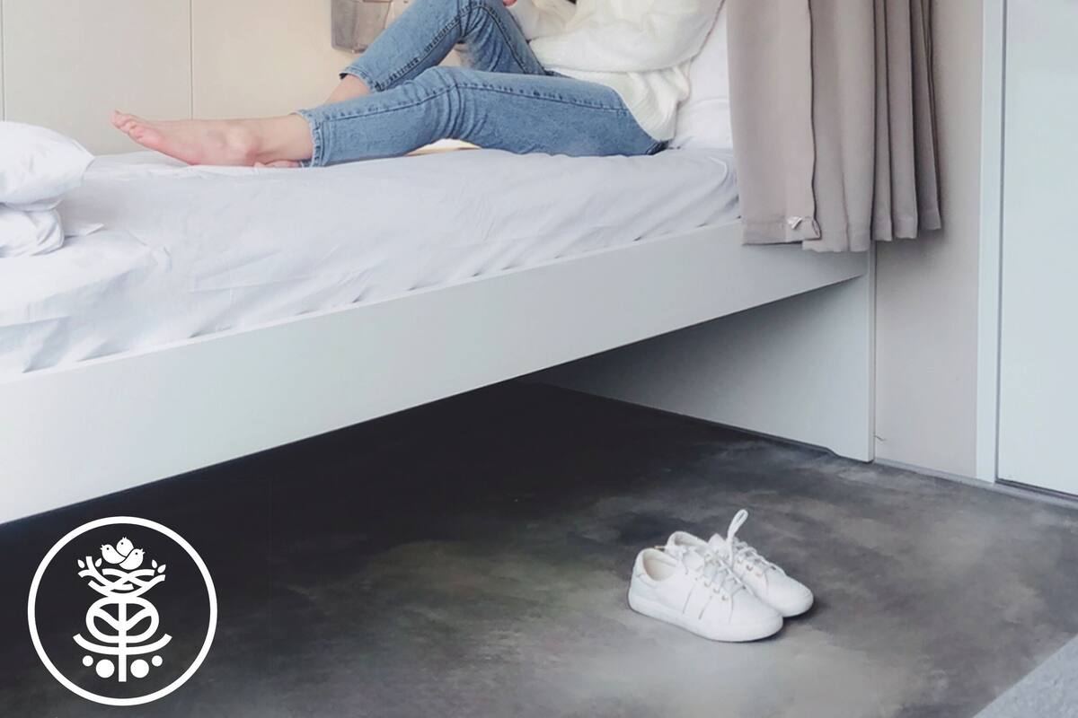 A person sitting on a bed in a room with a door and a curtain.