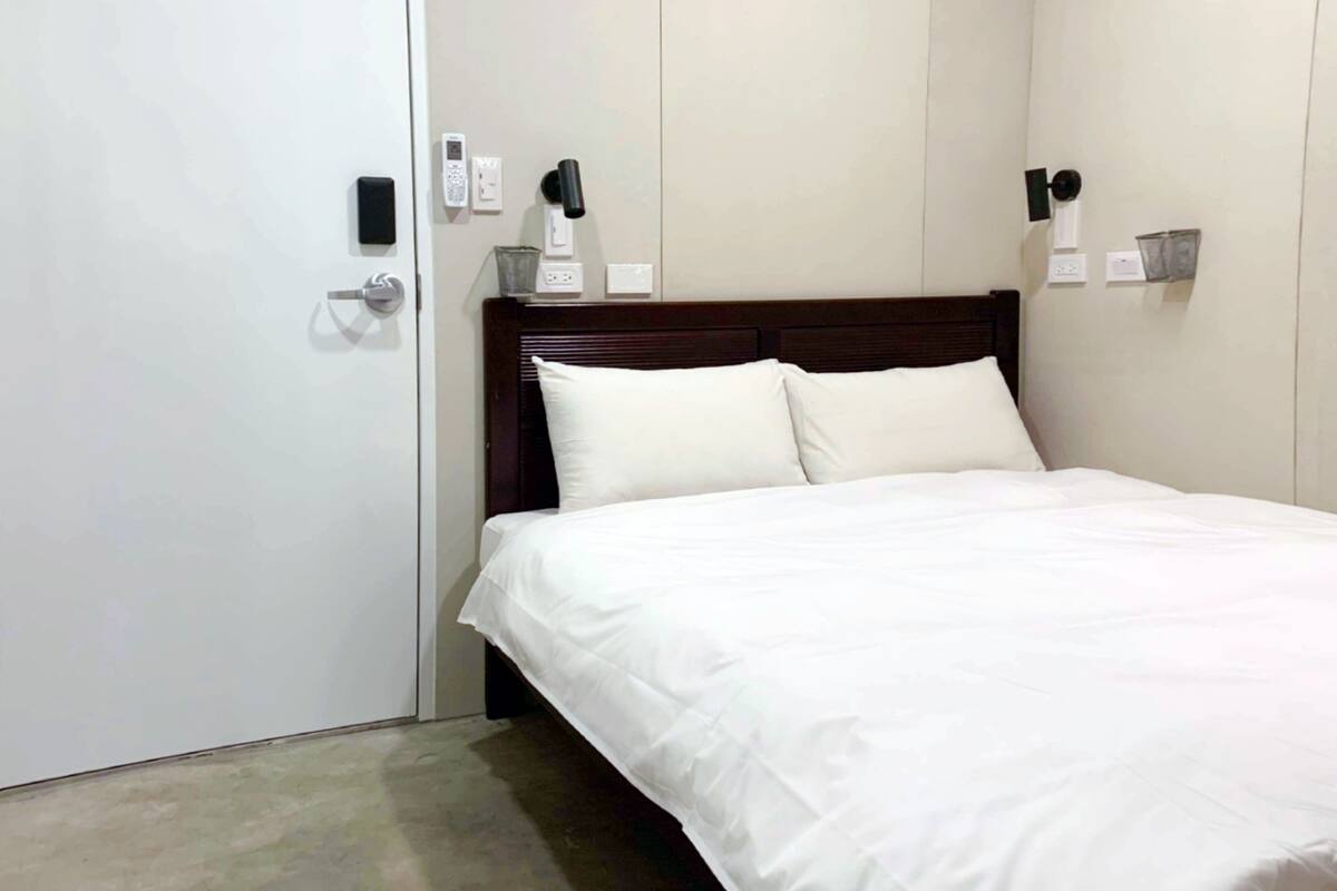 A hotel room with a bed, a wooden headboard, a white wall, and a door.