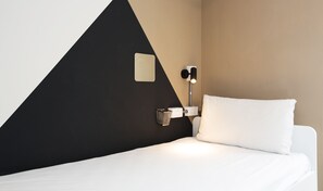 A modern hotel room with a bed, a wall-mounted light fixture, and a geometric wall design.