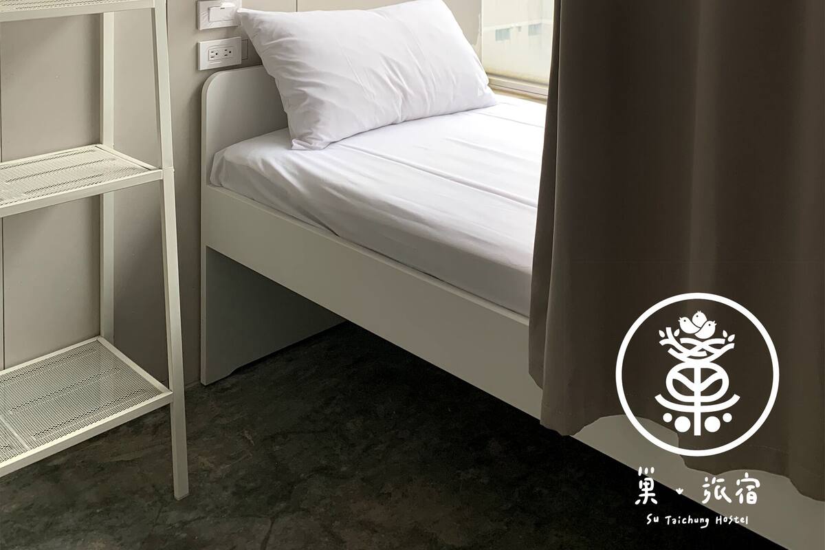 A minimalist hotel room with a bed, white shelves, and a wall-mounted light.