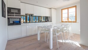 Una cocina moderna con armarios blancos, una estufa de acero inoxidable y un comedor con sillas blancas.