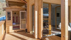 Una cabaña de madera con sauna, una puerta de cristal que da a un área de almacenamiento y una terraza de madera.