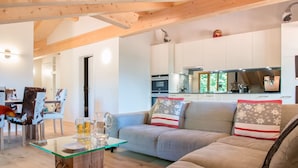 Una sala de estar moderna con una mesa de centro de vidrio, un sofá gris con cojines estampados y un techo de madera.