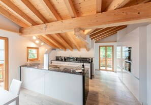 A modern kitchen with a central island, wooden beams, and a view to the outside.
