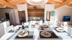 Un comedor con una mesa larga dispuesta para una comida, una chimenea al fondo y una cocina a la izquierda.