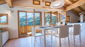 A dining area with a table set for four, large windows offering mountain views, and a chandelier.