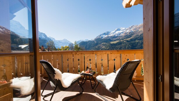 A balcony with two wicker chairs and a small table, overlooking a mountainous landscape.