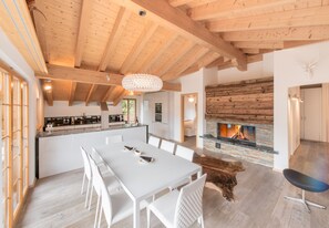 A modern kitchen with a central island, a dining area with white furniture, and a stone fireplace.