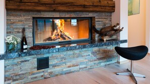 A fireplace with a stone facade, a black chair, and a bottle of wine on the mantel.