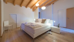 Un dormitorio moderno con una cama grande, suelo de madera y techo alto con vigas a la vista.
