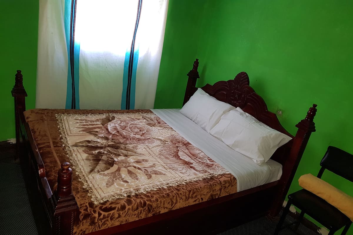 Un lit avec une couvre-lit à motifs floraux et des oreillers blancs, dans une pièce aux murs verts et dotée d’une tête de lit en bois.