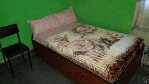 A single bed with a floral bedspread, a pillow, and a rolled towel. A black chair is positioned to the left of the bed. - Abrham Lalibela Home Stay (Lalibela)