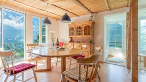 Un coin repas avec une table et des chaises en bois, un buffet avec des portes en verre et de grandes fenêtres donnant sur une vue imprenable sur les montagnes.