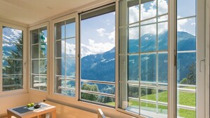 Une pièce dotée de grandes fenêtres donnant sur une vue sur les montagnes, une table en bois avec des pommes et un coussin bleu.