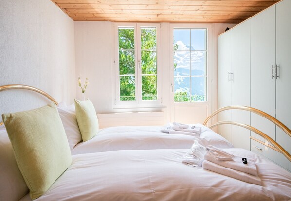 Une chambre avec une grande fenêtre, un lit recouvert de draps blancs et un plafond en bois.