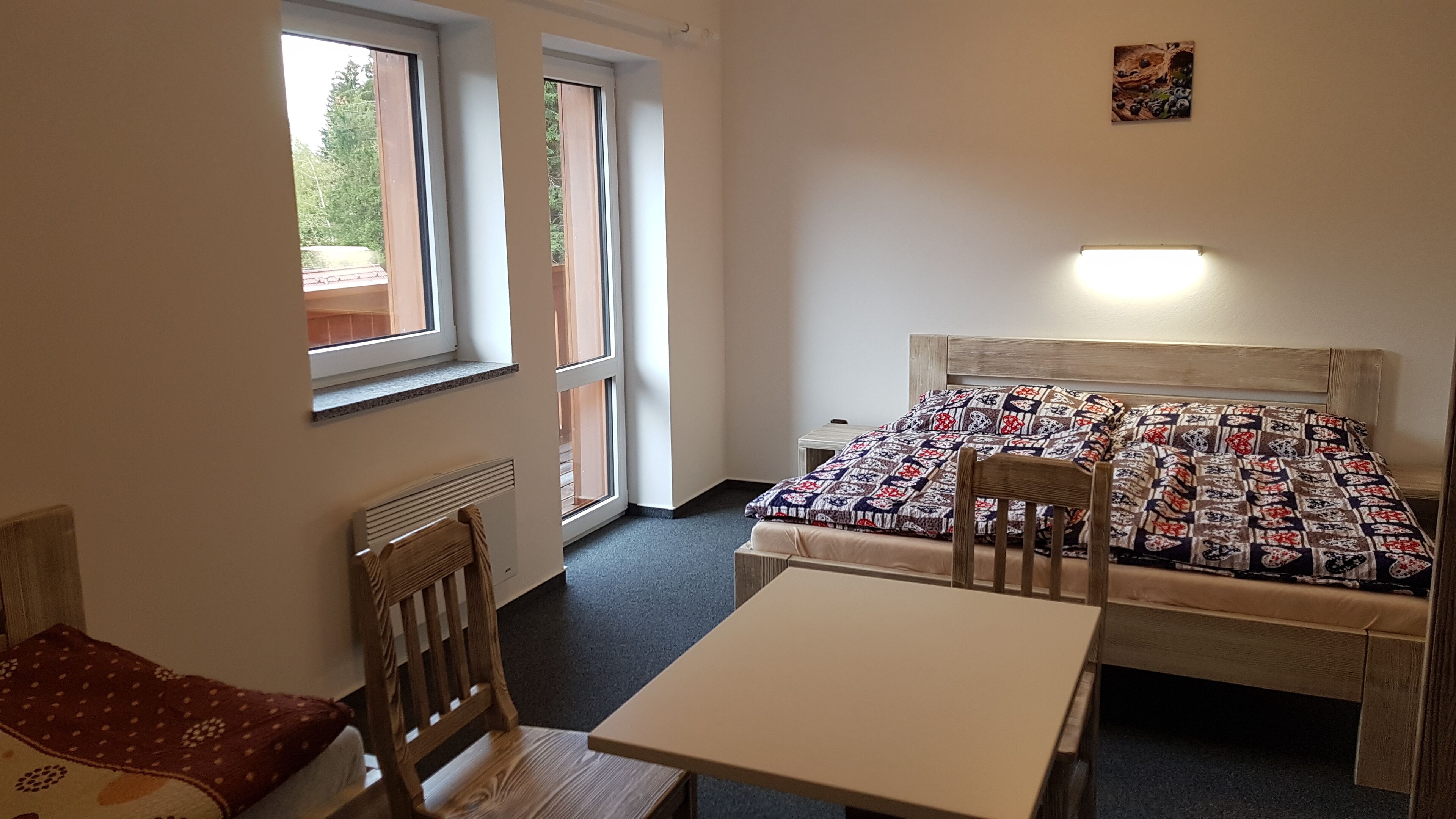 Una habitación pequeña y luminosa con una cama individual, una silla de madera, una mesa y un radiador.