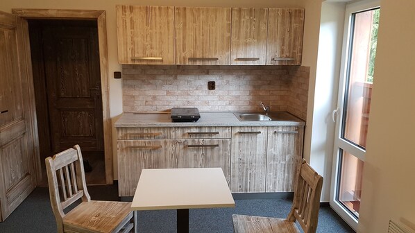 A compact kitchen with wooden cabinets, a built-in brick backsplash, a sink, and a table with two chairs.