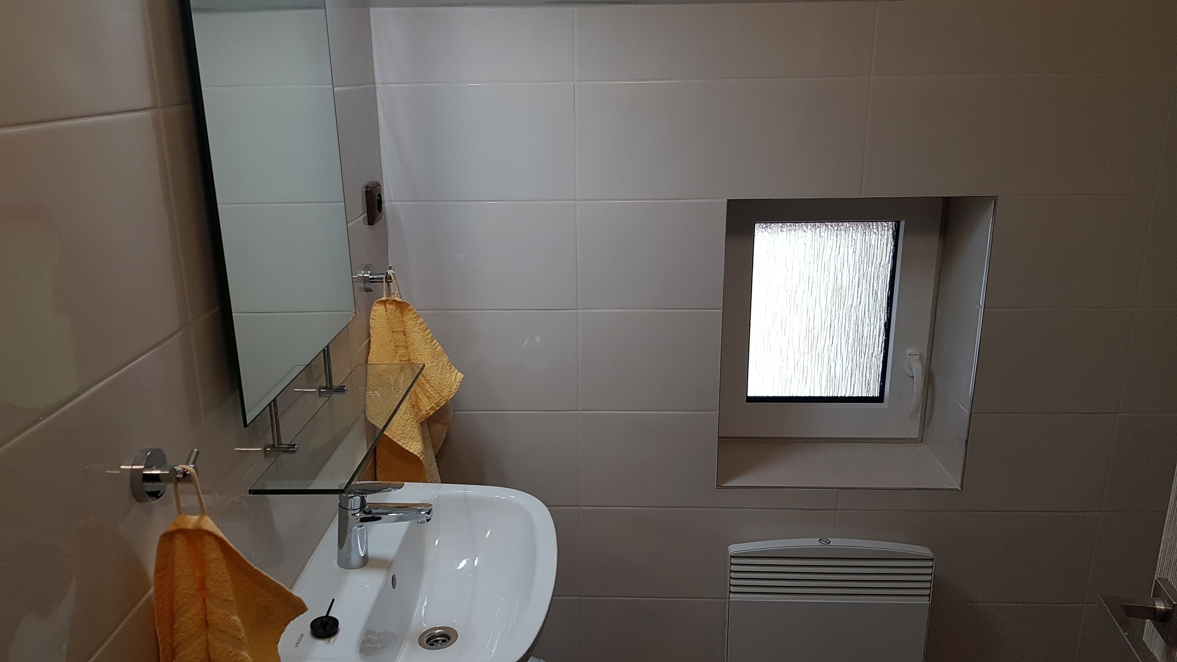 A bathroom with a white sink, a mirror, a towel rack, and a small window.