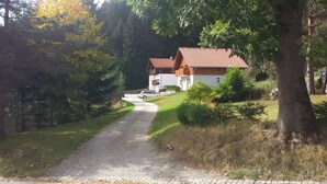 A gravel driveway leading to a row of two-story houses with red-tiled roofs, surrounded by trees and greenery. - Pension Pek (Kubova Hut)